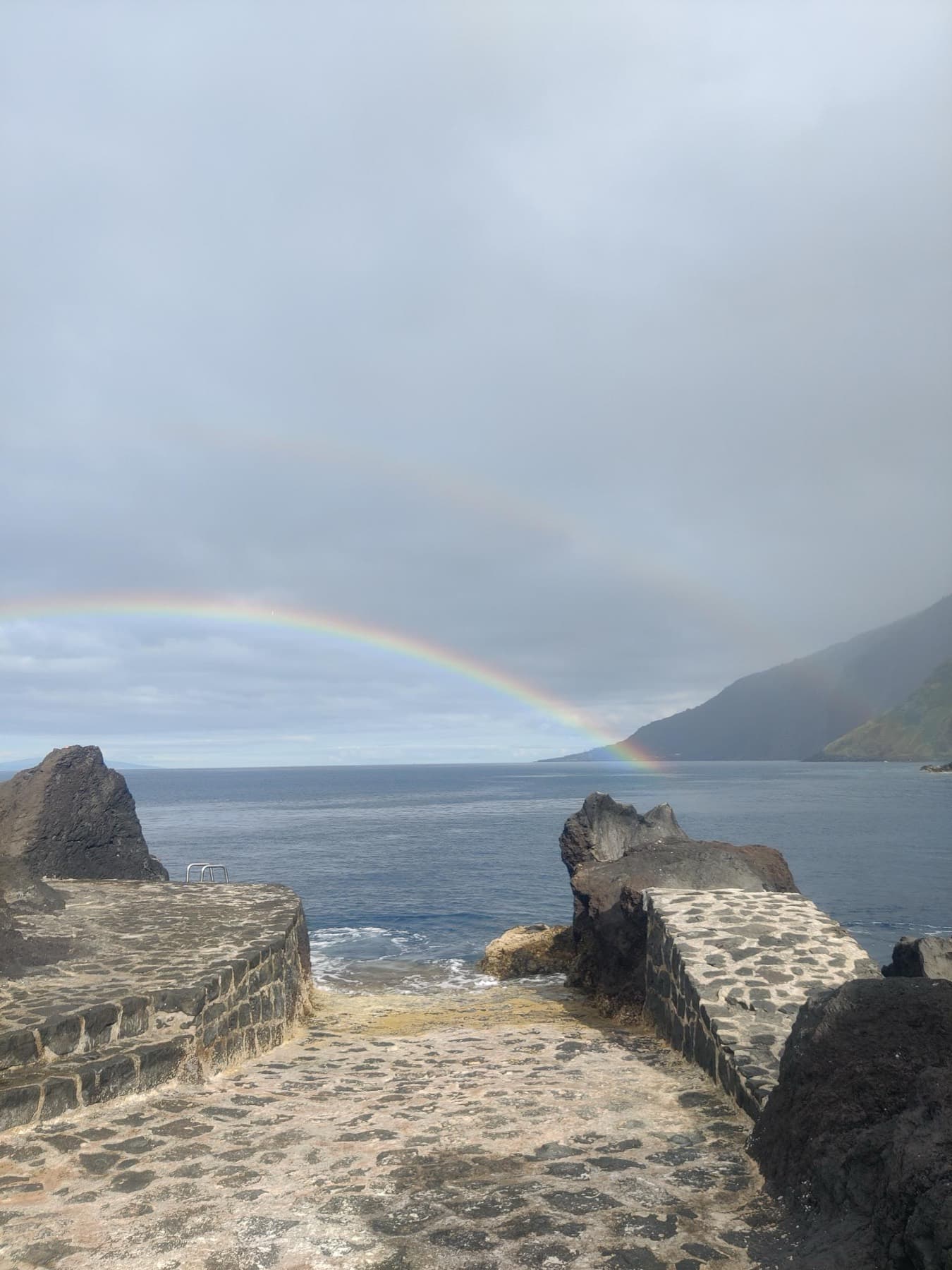 A rainbow over the ocean, seen from a stone pier